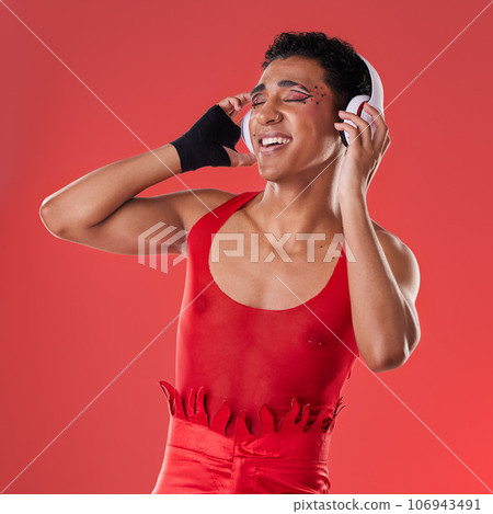Dance, music and gay man with headphones isolated on a red background in a studio. Freedom, streaming and dancing lgbt person listening to a podcast, radio and audio on a backdrop for entertainment 106943491