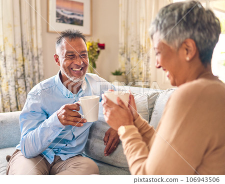 Coffee, laughing and a senior couple on a sofa in the home living room to relax while bonding in conversation. Smile, retirement or love with a mature married man and woman talking while drinking tea 106943506