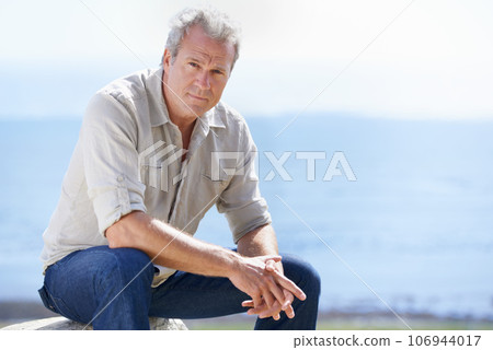 Years of rugged experience are reflected in his face. Portrait of a mature man sitting outdoors. 106944017