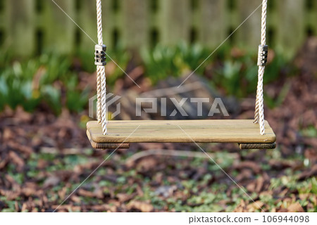 An empty wooden swing in a garden outside in the late afternoon with copyspace. A space to play in a backyard for active children wanting to have fun and play with copy space 106944098