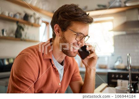 Technology, man on a phone call and happy in a kitchen for remote work at his home. Smile for online communication, connectivity or social networking and male person with smartphone talking. 106944184