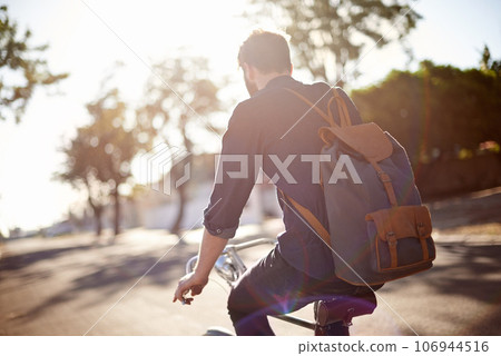 Bicycle, travel and back of man in street with lens flare for exercise, commute and cycling in morning. Transport, city and male cyclist on bike for eco friendly traveling, carbon neutral and journey Bicycle, travel and back of man in street with lens flare for exercise, commute and cycling in morning. Transport, city and male cyclist on bike for eco friendly traveling, carbon neutral and journey 106944516