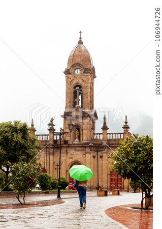 Woman walking with an umbrella at the beautiful central square aof the small town of Nobsa in a rainy day 106944726