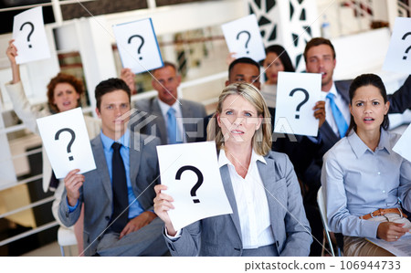 Stop leaving us in the dark. Shot of a group of businesspeople holding up signs with question marks on them during a work presentation. 106944733