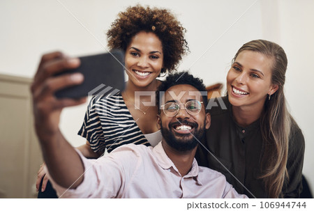 Group of office friends taking a happy selfie using a phone in business place. Cheerful, excited and joyful colleagues, work team and coworkers taking fun photos together. 106944744