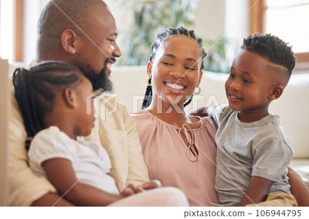 Relaxed african american family smiling while sitting on the couch. Shot of a young happy black couple relaxing on the sofa while talking to their two young adorable kids at home 106944795