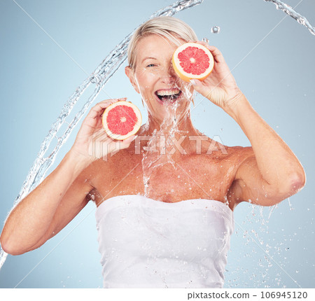 Woman, studio portrait and grapefruit with water splash, smile and happy for wellness by blue background. Senior model, organic citrus fruit and vitamin c for health, nutrition and self care process 106945120