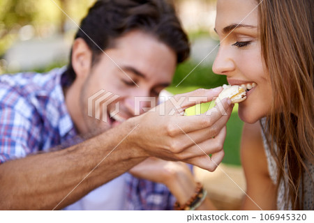 Couple picnic, romantic and feeding on grass lawn with happiness, kindness and love on valentines date. Man, woman and eating together at nature park with food for bonding, romance and care by trees 106945320