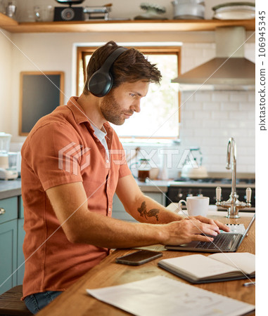 Remote work, laptop and headphones, man in kitchen typing email, social media post or networking for online job. Technology, streaming and freelancer on internet writing blog or article with music. Remote work, laptop and headphones, man in kitchen typing email, social media post or networking for online job. Technology, streaming and freelancer on internet writing blog or article with music. 106945345