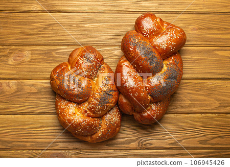 Two reshly baked Challah bread covered with poppy and sesame seeds, top view on rustic wooden background, traditional festive Jewish cuisine 106945426