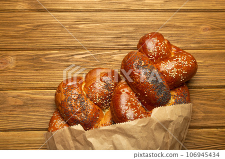 Freshly baked Challah bread covered with poppy and sesame seeds in a paper bag, top view on rustic wooden background, traditional festive Jewish cuisine 106945434
