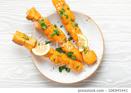 Grilled barbecue salmon skewers seasoned with green parsley and lemon on ceramic plate on white wooden rustic table background top view, healthy eating 106945441