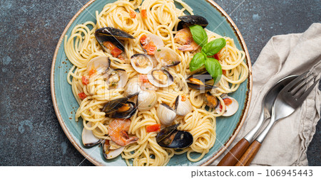 Italian seafood pasta spaghetti with mussels, shrimps, clams in tomato sauce with green basil on plate on rustic blue concrete background top view. Mediterranean cuisine Italian seafood pasta spaghetti with mussels, shrimps, clams in tomato sauce with green basil on plate on rustic blue concrete background top view. Mediterranean cuisine 106945443