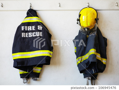 Firefighter, uniform and clothing hanging on wall rack at station for fire fighting protection. Fireman gear, rescue jacket and helmet with reflector for emergency services, equipment or department 106945476