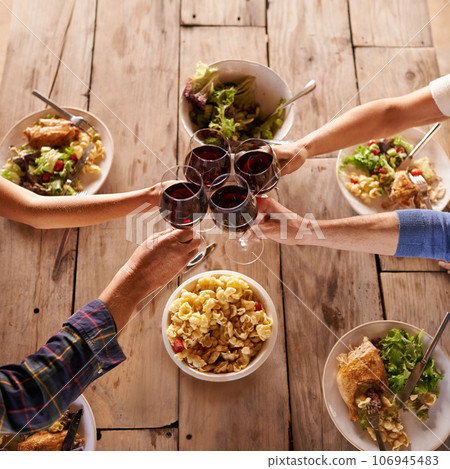 Hands, toast with wine glasses and food with cheer for celebration at lunch. Top view of event, congratulations or success and friends or family sharing a meal or dish together at table with drinks 106945483