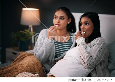 Popcorn, eating and women or friends with horror movies, scary show and sleepover on bed, streaming service or television. Gen z people relax in bedroom for drama TV film, home cinema or subscription 106945706