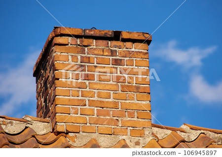 Copy space with a chimney on the rooftop of a house or building against a blue sky background. Brick construction of an exterior escape chute for ventilation of air and smoke from a fireplace or oven Copy space with a chimney on the rooftop of a house or building against a blue sky background. Brick construction of an exterior escape chute for ventilation of air and smoke from a fireplace or oven 106945897
