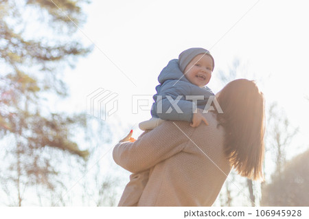 Happy family outdoor. Mother embracing her child outdoor. Mom lifting in air little toddler child son. Woman and little baby boy resting walking in park. Mother hugs baby with love care 106945928