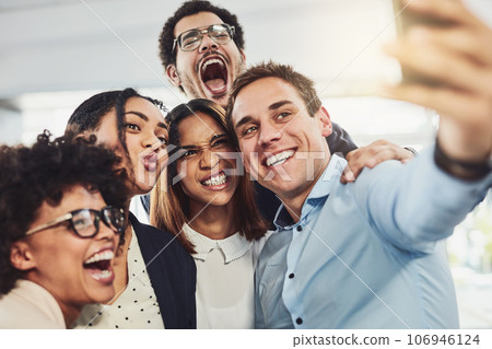 Teamwork, playful and selfie while a group of cheerful businesspeople making funny faces together for a social media post. Faces of a happy and fun team standing together in a creative office Teamwork, playful and selfie while a group of cheerful businesspeople making funny faces together for a social media post. Faces of a happy and fun team standing together in a creative office 106946124