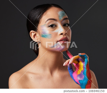 Woman, beauty and portrait with rainbow hand paint art on face in studio with glow. Creative skin and makeup on female aesthetic model serious on gray background for lgbtq color inspiration on hands Woman, beauty and portrait with rainbow hand paint art on face in studio with glow. Creative skin and makeup on female aesthetic model serious on gray background for lgbtq color inspiration on hands 106946150