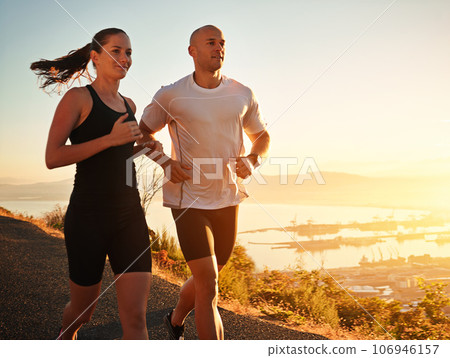 Running is part of their daily routine. Shot of a young couple running together along a road. Running is part of their daily routine. Shot of a young couple running together along a road. 106946157