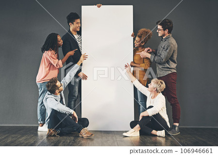 A diverse group of people holding a blank white board or poster and showing advertising copy space. A team or friends marketing a placard banner standing and sitting together for a promotion 106946661