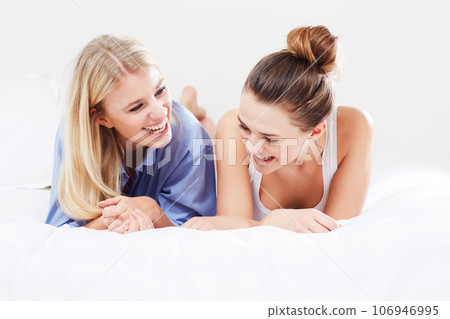 Funny, relax and friends in bed laughing together as happiness isolated in a studio white background. Smile, happy and female people or women laugh at a joke and feeling excited in a bedroom Funny, relax and friends in bed laughing together as happiness isolated in a studio white background. Smile, happy and female people or women laugh at a joke and feeling excited in a bedroom 106946995