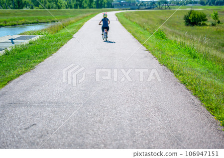 focus on near pavement with blurred distant child wearing a helmet while riding a bike on a park path  106947151