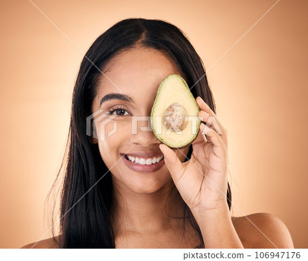 Happy, face and woman with avocado for skincare isolated on a brown background in studio. Portrait, fruit and model with food for nutrition, skin health and vegan diet, omega 3 or natural cosmetics 106947176
