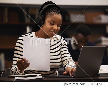 Woman, studying and headphones in library for research, documents and computer research or planning in university. African student reading paper, listening to music or laptop for focus and e learning Woman, studying and headphones in library for research, documents and computer research or planning in university. African student reading paper, listening to music or laptop for focus and e learning 106947498