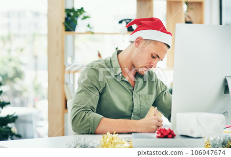Christmas, computer and businessman writing at a desk, thinking and planning in his office alone. Festive, season and employee working to meet deadline on xmas eve, write list, note or reminder Christmas, computer and businessman writing at a desk, thinking and planning in his office alone. Festive, season and employee working to meet deadline on xmas eve, write list, note or reminder 106947674
