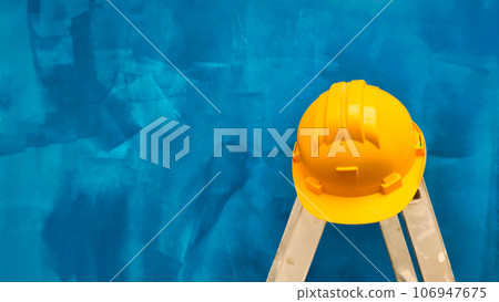 a ladder with a hard hat on a background of a blue wall a ladder with a hard hat on a background of a blue wall 106947675