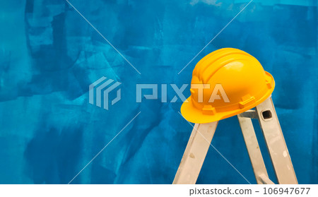 a ladder with a hard hat on a background of a blue wall a ladder with a hard hat on a background of a blue wall 106947677