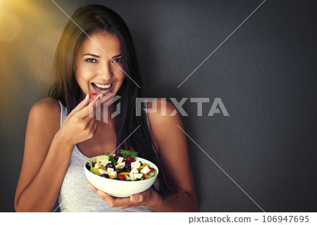 Woman is eating a tomato from salad, portrait and healthy food with nutrition and vegetables on wall background. Happy, vegan and health, female model on diet to lose weight and mockup space Woman is eating a tomato from salad, portrait and healthy food with nutrition and vegetables on wall background. Happy, vegan and health, female model on diet to lose weight and mockup space 106947695