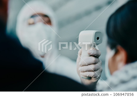 Medical healthcare worker, scanning temperature of covid patient for safety against virus pandemic, wearing protective suit. Doctor in hazmat suit checking with thermometer for potential outbreak. 106947856