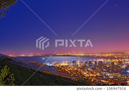 Signal Hill in Cape Town South Africa with copyspace against dark night sky background and the view of a coastal city. Scenic panoramic landscape of lights illuminating an urban skyline along the sea 106947916