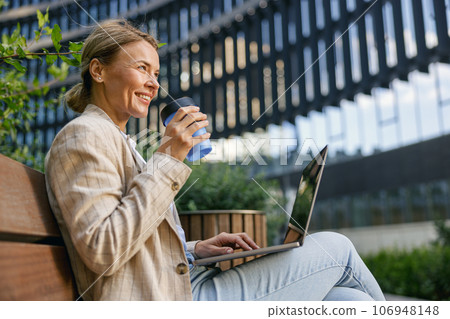Businesswoman drinking coffee and work on laptop outside of office. Distance work concept Businesswoman drinking coffee and work on laptop outside of office. Distance work concept 106948148
