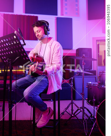 Musician, headphones or guitar in neon studio, recording production or performance on radio mic, label or band concert. Guitarist, artist or man playing on strings instrument in night light practice 106948395