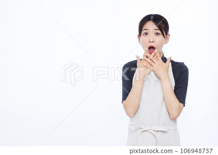 A housewife in her 30s looking surprised in front of a white background A housewife in her 30s looking surprised in front of a white background 106948737