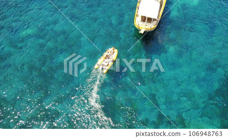 People on boat from above, sailing in Greece and summer sun on ocean holiday, relax in freedom and nature. Yacht vacation, aerial view of travel and tropical cruise on sea adventure to Greek island. People on boat from above, sailing in Greece and summer sun on ocean holiday, relax in freedom and nature. Yacht vacation, aerial view of travel and tropical cruise on sea adventure to Greek island. 106948763