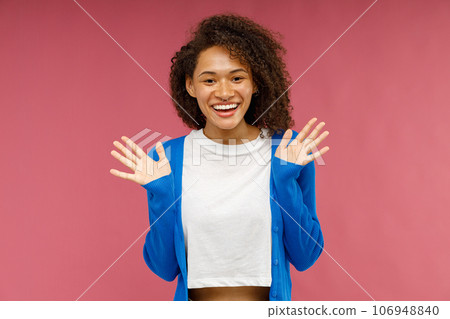 Surprised woman with raised hands looks camera while standing over red studio background 106948840