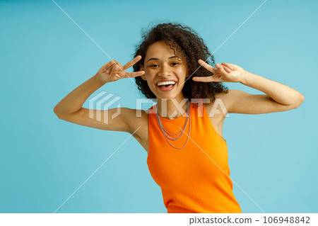 Happy woman standing over blue background smiling with happy face doing victory sign with fingers 106948842