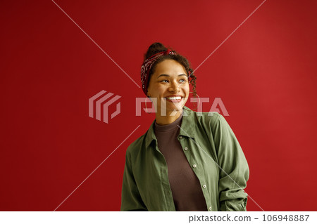 Stylish woman looks away with smile while standing on red studio background Stylish woman looks away with smile while standing on red studio background 106948887