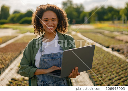 Woman gardener working on laptop while sitting on background of shop plants center 106948903