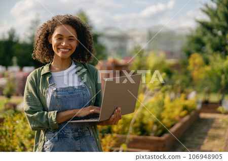 Woman gardener working on laptop while sitting on background of shop plants center Woman gardener working on laptop while sitting on background of shop plants center 106948905