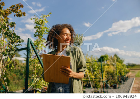 Cheerful woman gardener making notes in clipboard while standing in garden center 106948924