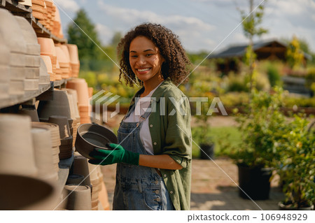 Woman gardener standing near shelves full of empty flowers pots in garden center Woman gardener standing near shelves full of empty flowers pots in garden center 106948929