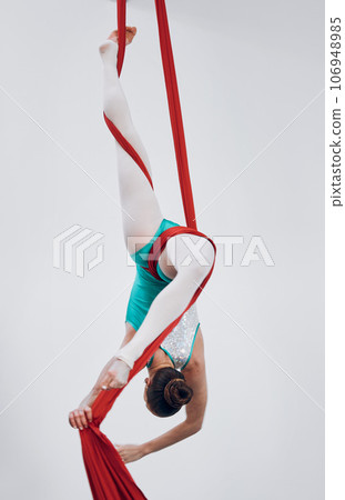 Performance, acrobat and aerial silk with a woman in air for gymnastics, sports and balance. Athlete person, dancer or gymnast hanging on red fabric and white background with space, art or creativity 106948985