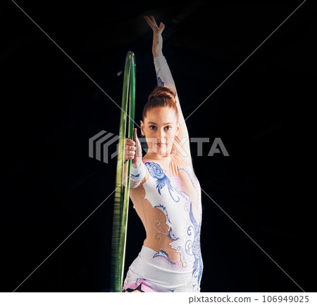 Portrait, dance with a gymnastics hoop and a woman in the gym for a performance showcase or practice. Fitness, training and concert with a female athlete on a dark background for routine or recital Portrait, dance with a gymnastics hoop and a woman in the gym for a performance showcase or practice. Fitness, training and concert with a female athlete on a dark background for routine or recital 106949025