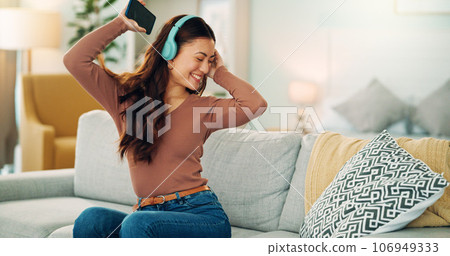 Phone, dancing and woman streaming music via headphones to relax with freedom on the weekend at home. Dance, excited and happy girl enjoys listening to a radio song or audio on an online subscription 106949333